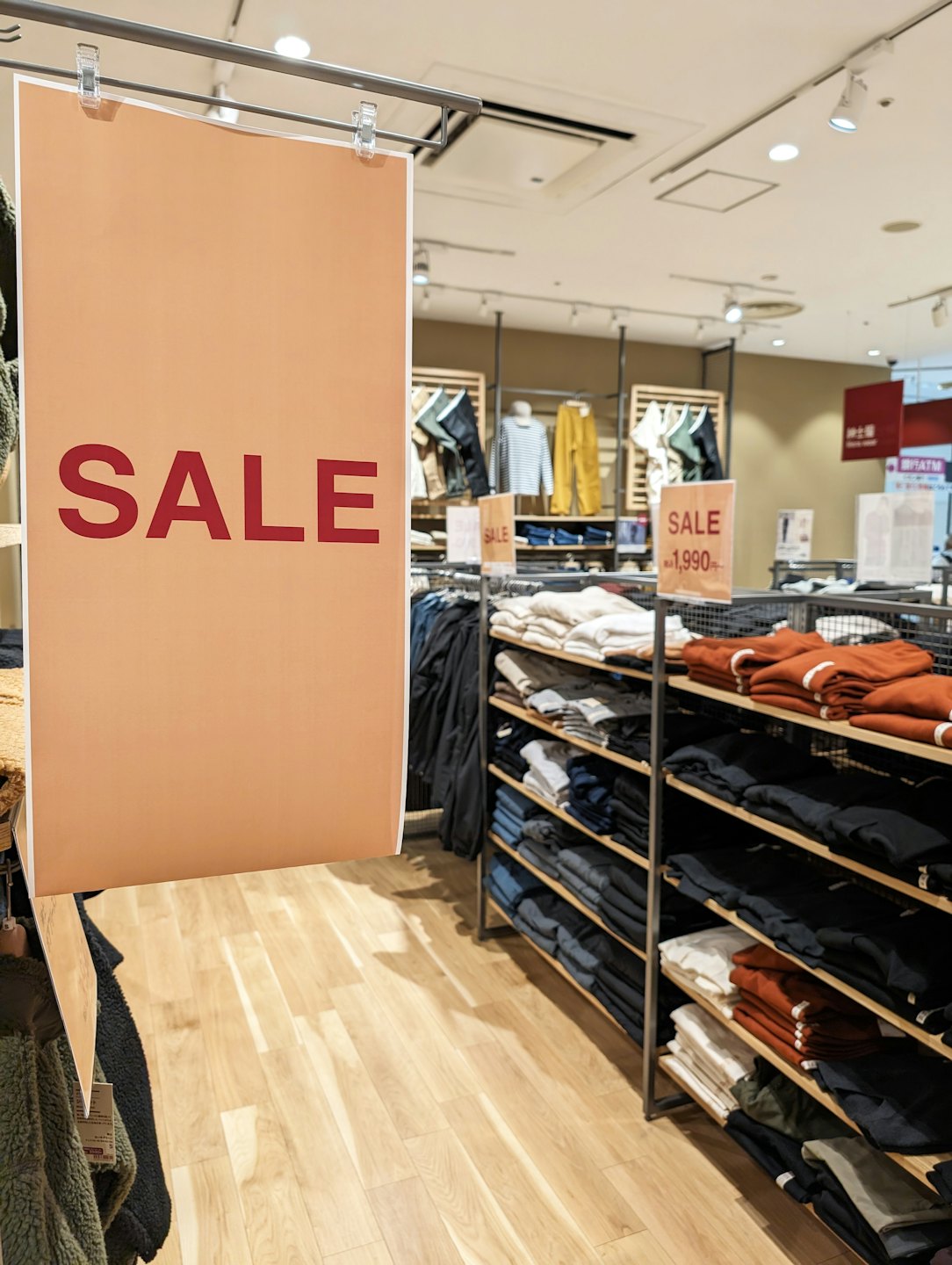 Peach 'SALE' sign in a clothing store with folded clothes.